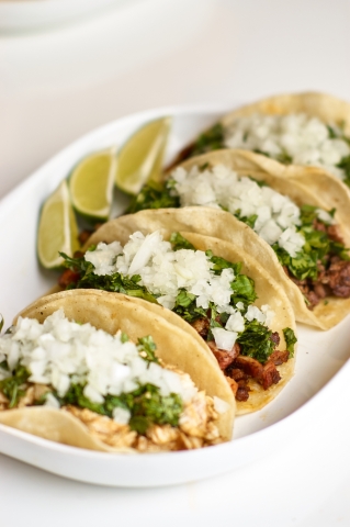 Four tacos on a plate with lime 