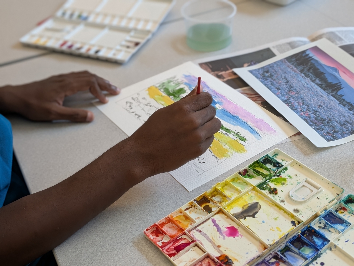 Hands painting with watercolor supplies and a brush